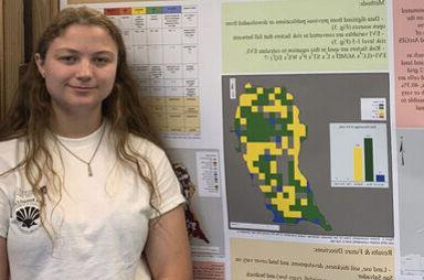 A female student stands with her Bahamas research poster