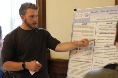 A male student references points within his research on a poster board during the Student Research Conference